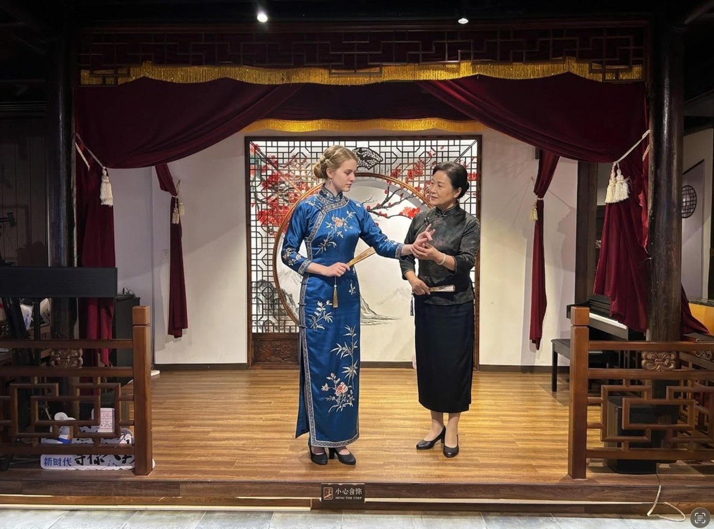 A guest in a blue opera costume learning a gesture with an instructor at Zhao's Workshop